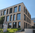 Modernes dreistöckiges Bürogebäude aus hellem Backstein mit großen Fensterfronten und Firmenschild im Vordergrund.