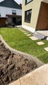Frisch verlegter Rollrasen mit Trittplatten aus Naturstein und einer gepflasterten Mähkante neben einem modernen Wohnhaus.