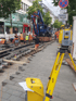 Bauarbeiter verlegen Straßenbahnschienen auf einer städtischen Straße mit einem gelben Vermessungsgerät im Vordergrund.