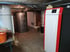 Heizraum mit Windhager-Pelletkessel, zwei Warmwasserspeichern und freiliegenden Rohren an der Decke.