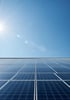 Solarmodule unter einem strahlend blauen Himmel mit der Sonne links oben.