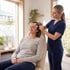 A medical professional in blue scrubs applies EEG electrodes to the forehead and temple of a seated woman with closed eyes.