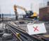 Ein Schild mit rotem X auf Baustahl vor einem Bagger auf einer Baustelle.