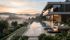 Moderne Villa mit Infinity-Pool und Terrasse bei Sonnenuntergang, umgeben von Hügeln und Nebel.
