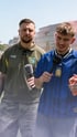 Ein lachender Mann mit Bart telefoniert mit einem Smartphone und hält sich die Ohren zu.
