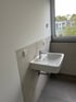 Ein weißes Waschbecken mit Chromarmatur in einem Raum mit grauen Fliesen und einem Fenster.
