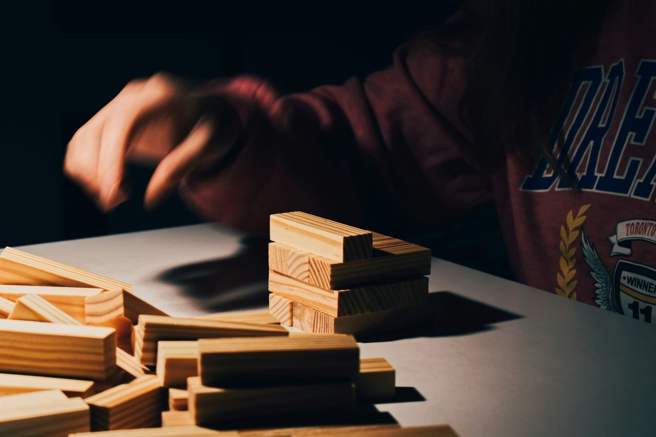 Eine Hand stapelt Holzklötze zu einem Turm auf einem Tisch im Seitenlicht