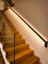 Holztreppe mit Glasgeländer und beleuchtetem Handlauf an weißer Wand.