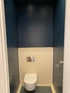 Toilette mit WC-Sitz, Spülkastenverkleidung in Cremefarbe und dunkelblauen Wänden.