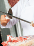Metzger schärft ein Messer an einem Wetzstahl über einem Stück rohem Fleisch.