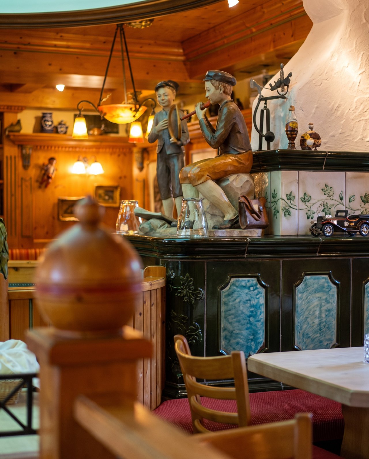 Geschnitzte Holzfiguren auf dem gekachelten Ofen im Gastraum
