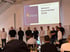 Das Team steht auf der Bühne vor der Leinwand mit dem Schriftzug Versuro Sommerfest 2026, davor sitzt das Publikum