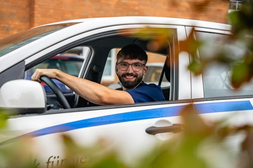 Ein Mann im blauen Kasack sitzt am Steuer eines Diakonie-Fahrzeugs.