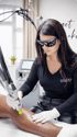 Eine Frau mit Schutzbrille und Handschuhen führt eine Laser-Haarentfernung an einem Bein durch, das mit weißen Linien markiert ist.
