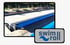 Blauer Swimroll Poolrollladen bedeckt teilweise ein Schwimmbecken; Liegestühle stehen am Poolrand.