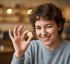 Junge Frau mit Locken zwinkert und hält eine goldene Münze zwischen Daumen und Zeigefinger.