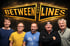Fünf lächelnde Männer stehen vor dunklem Hintergrund unter dem goldenen Schriftzug „BETWEEN THE LINES“.
