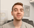 Ein junger Mann mit Bart und grauen T-Shirt blickt direkt in die Kamera, YouTube-Play-Buttons im Hintergrund.