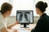 Ärztin zeigt Patientin auf einem Monitor eine Röntgenaufnahme der Brust.