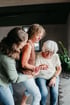 Zwei jüngere Frauen unterstützen eine sitzende Seniorin beim Aufstehen und halten dabei ihre Hände.