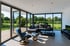 Modernes Wohnzimmer mit großer Fensterfront, Ledersofa, Sessel und Blick auf einen grünen Garten.