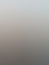 Junge Frau lächelt vor einem ruhigen Gewässer mit einem hellen Himmel bei Sonnenuntergang.