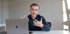Junger Mann sitzt vor Laptop und gestikuliert mit den Händen.