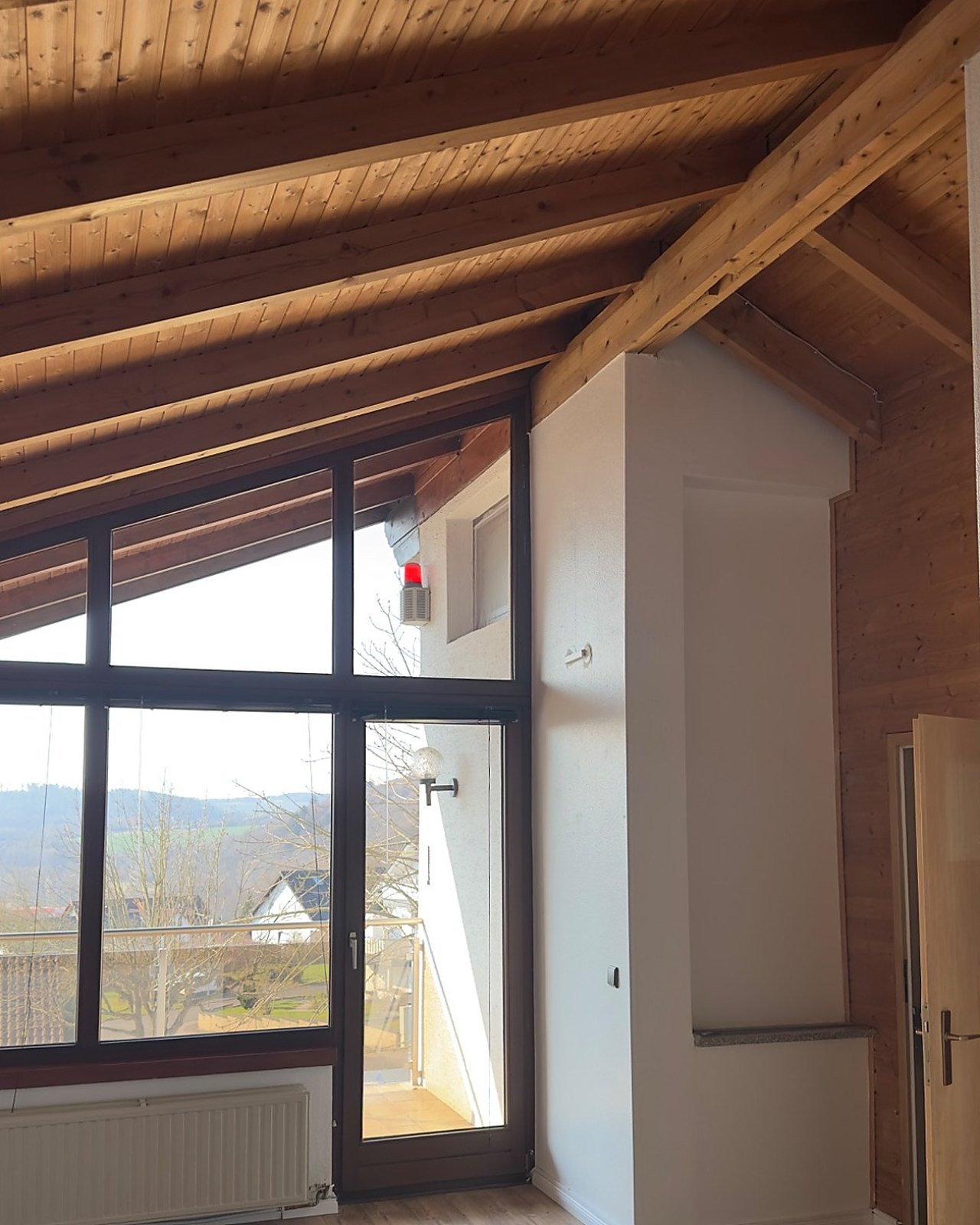 Innenansicht eines Dachraums mit sichtbarer Holzkonstruktion und großflächiger Verglasung.