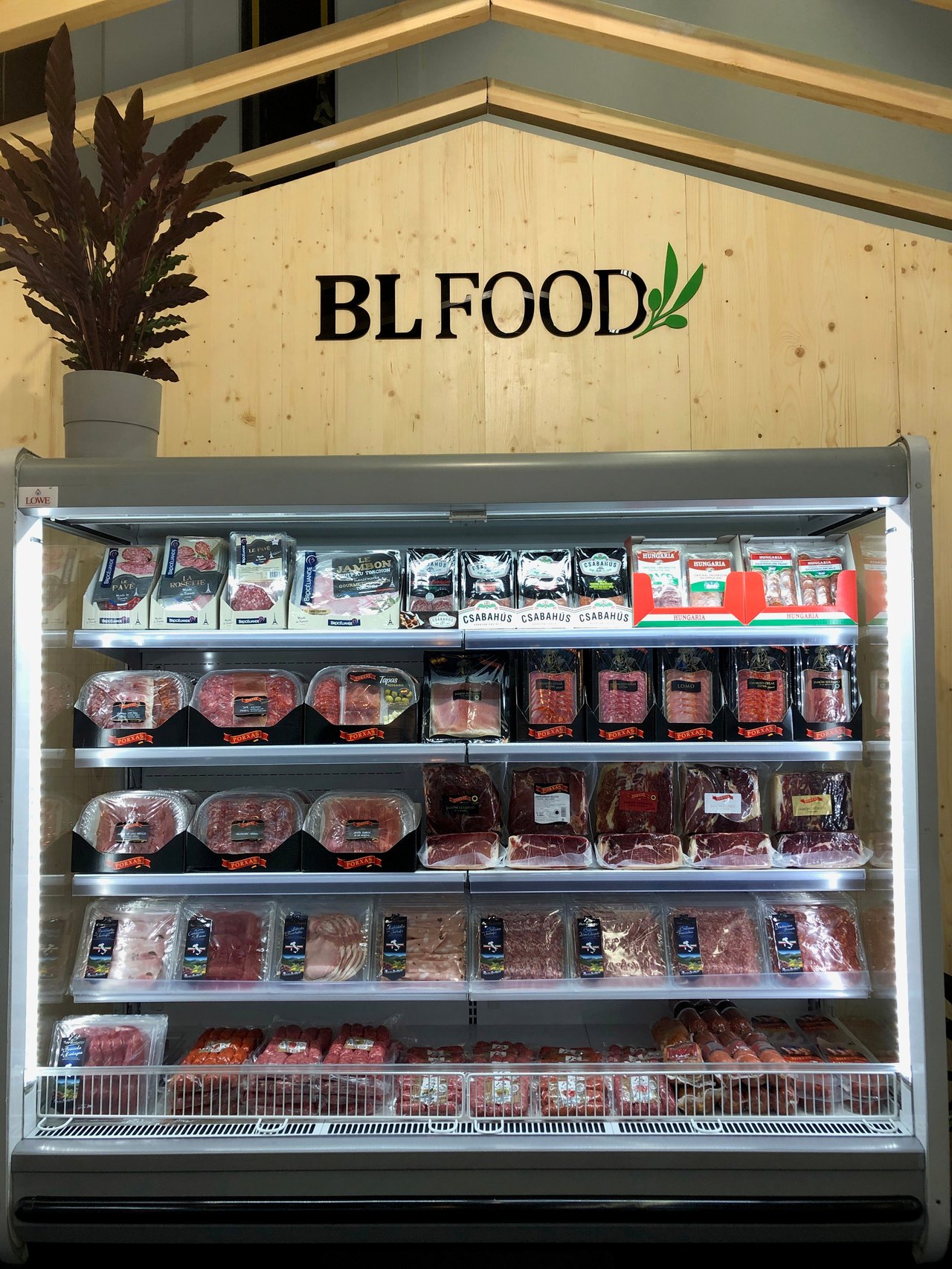Kühlregal von BL Food gefüllt mit verschiedenen abgepackten Fleisch- und Wurstwaren vor einer hellen Holzwand.