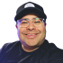 Man in a black baseball cap and clear-framed glasses smiling at the camera.