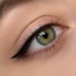 Nahaufnahme eines grünen Auges mit einem scharfen schwarzen Eyeliner-Flügel und langen Wimpern.