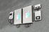 Zwei weiße Energiespeicher mit blauen Blitzsymbolen und ein Elektroauto-Ladegerät sind an einer grauen Backsteinwand montiert.