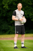 Ein Mann in Sportkleidung hält einen Fußball auf einem grünen Feld.