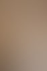 Lächelnde Frau mit lockigem Haar und Brille trägt eine beige Bluse und weiße Hose in einem hellen Raum mit Zimmerpflanze.