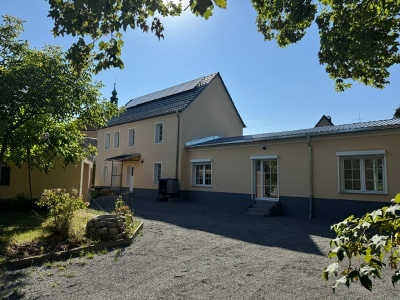 Einfamilienhaus mit gelber Fassade und Solaranlage auf dem Dach, davor die Hofeinfahrt