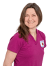 Lächelnde Frau mit braunen Haaren in einem lila Poloshirt mit dem Logo der Zahnarztpraxis Dr. med. dent. Priehn.