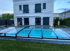 Hinterhof eines weißen Hauses mit einem abgedeckten Pool und grünem Rasen.