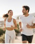 Smiling man and woman jogging on a path beside the ocean