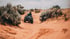 Person on a black ATV riding through a sandy desert path with green shrubs on either side.