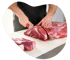 Ein Metzger schneidet mit einem Messer ein großes Stück rohes Rindfleisch auf einem weißen Schneidebrett.