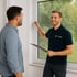 Berater erklärt einem Kunden vor Ort die Vorteile und Funktionsweise eines Fliegengitters am Fenster.