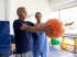 Physical therapist assists an older man holding an exercise ball