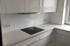 Moderne, weiße Küche mit Induktionskochfeld, Dunstabzugshaube und Steckdosen.