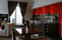 Heller Hotelzimmer-Loungebereich mit roter Akzentwand, Buffet, Esstisch und Blick auf einen Balkon.