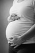 Schwarz-weiß-Aufnahme einer schwangeren Frau, die ihren Bauch mit beiden Händen hält.