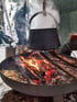 Ein großer schwarzer Topf hängt über einem Lagerfeuer in einer Metallschale, in der Schnee liegt.