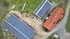 Draufsicht auf einen Bauernhof mit zwei Scheunendächern, die vollständig mit Solarpaneelen bedeckt sind.