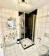Helles Badezimmer mit weißen Fliesen, Waschbecken, Dusche und Toilette.