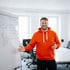Dennis Dittrich im orangefarbenen Hoodie gestikuliert vor einem Whiteboard mit Diagrammen und Notizen. *KI-Generiert