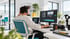 Ein Mann mit Kopfhörern bearbeitet ein Video an einem PC-Monitor in einem hellen, modernen Büro mit Kamera-Equipment.